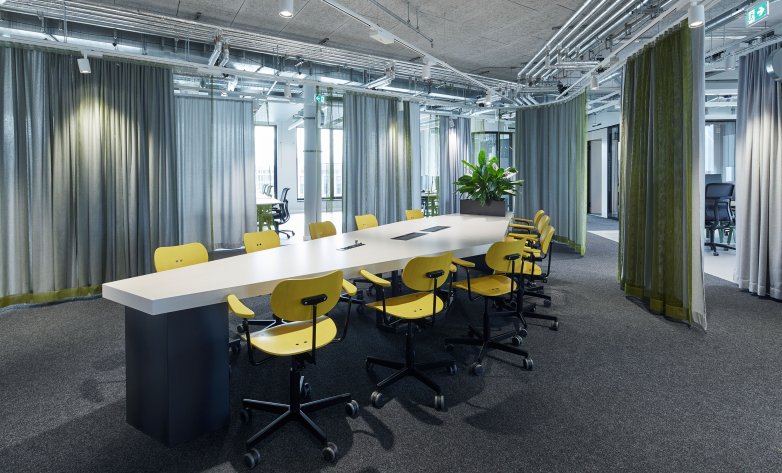 Mit Vorhängen abtrennbarer Besprechungsraum, großer Tisch mit gelben Stühlen