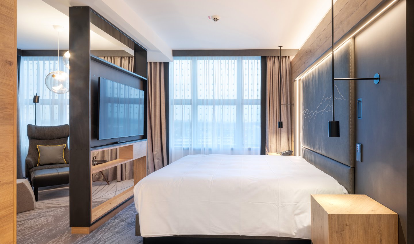 Luxussuite mit großem Bett, designer Möbel und freistehenden Fernseher in Holzkonstruktion - Hilton Hotel Munich Airport