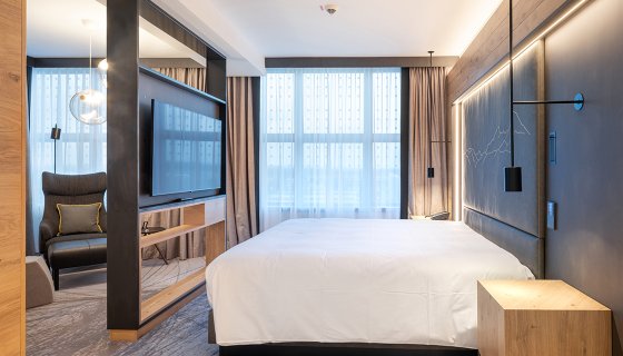 Luxussuite mit großem Bett, designer Möbel und freistehenden Fernseher in Holzkonstruktion - Hilton Hotel Munich Airport